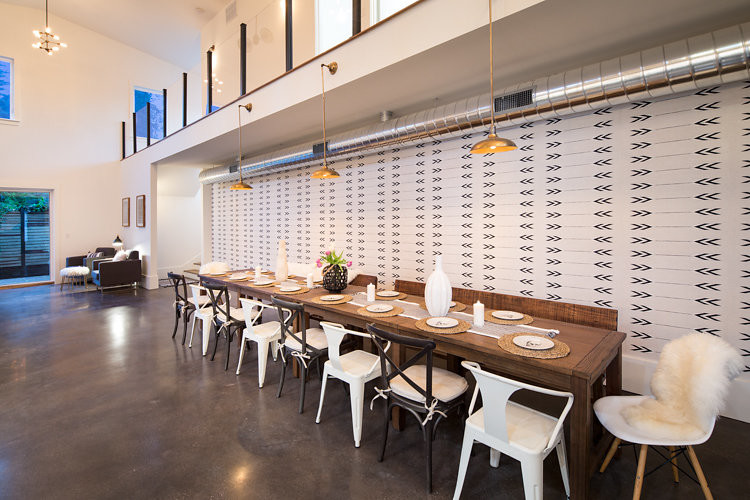 Cette image montre une grande salle à manger ouverte sur la cuisine urbaine avec un mur beige, sol en béton ciré, une cheminée ribbon et un manteau de cheminée en métal.