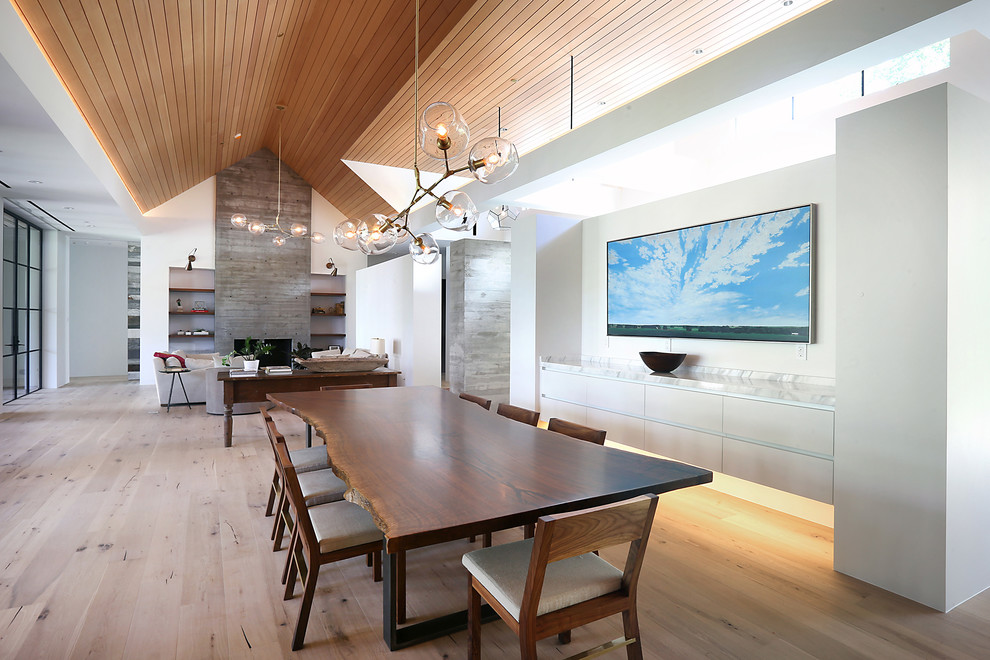 Cette photo montre une salle à manger ouverte sur le salon tendance de taille moyenne avec un mur blanc, un sol en bois brun, un sol marron, une cheminée standard et un manteau de cheminée en bois.