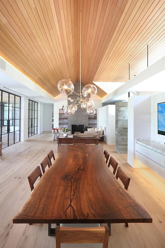 Inspiration pour une salle à manger ouverte sur le salon design de taille moyenne avec un mur blanc, un sol en bois brun, une cheminée standard, un manteau de cheminée en bois et un sol marron.