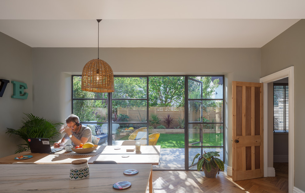 Cette image montre une salle à manger ouverte sur la cuisine avec un mur gris et parquet clair.