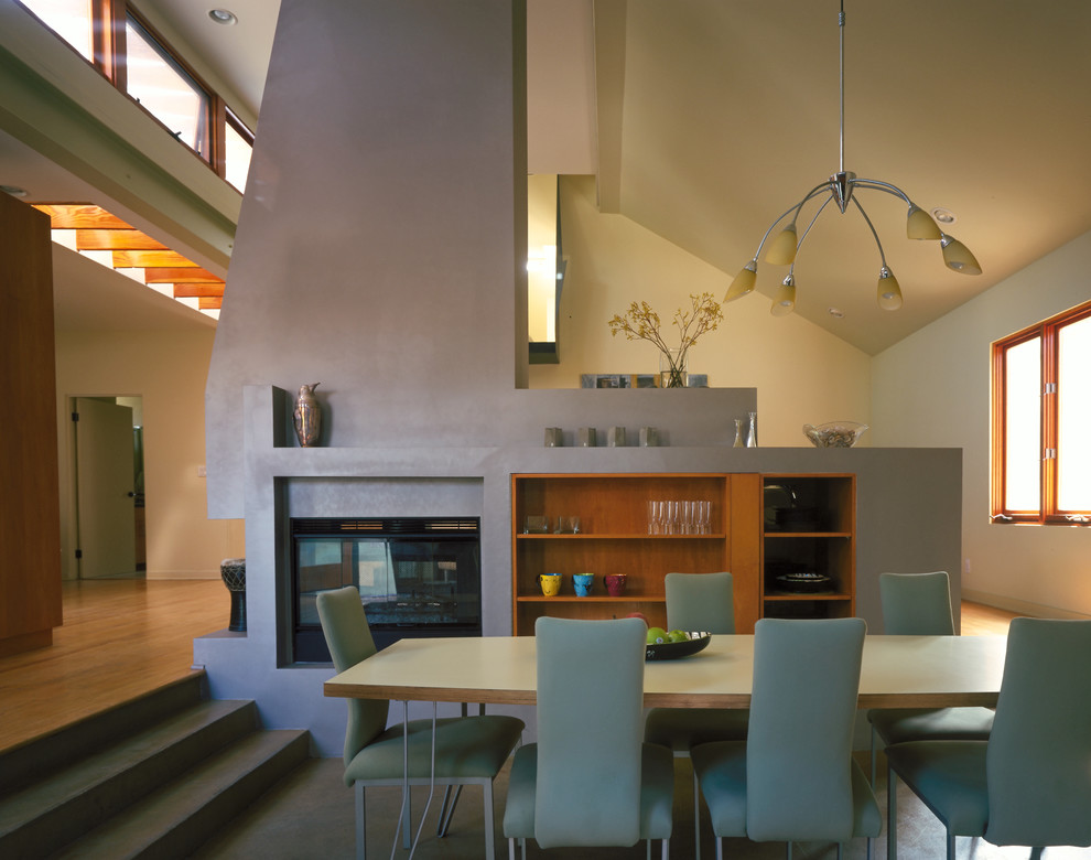 Cette photo montre une salle à manger ouverte sur le salon tendance de taille moyenne avec un mur vert, sol en béton ciré, une cheminée double-face et un manteau de cheminée en plâtre.