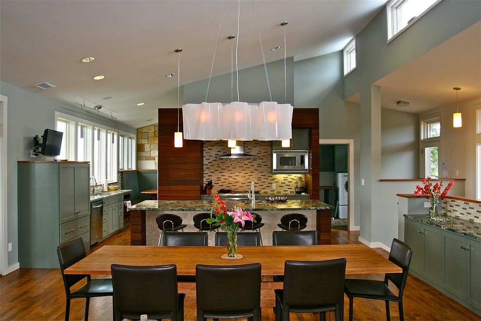 Cette image montre une salle à manger ouverte sur le salon design de taille moyenne avec un mur vert, un sol en bois brun et un manteau de cheminée en pierre.