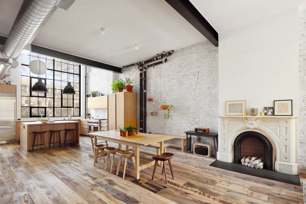 Cette image montre une grande salle à manger ouverte sur la cuisine urbaine avec un mur blanc, un sol en bois brun, une cheminée standard, un manteau de cheminée en bois et un sol marron.