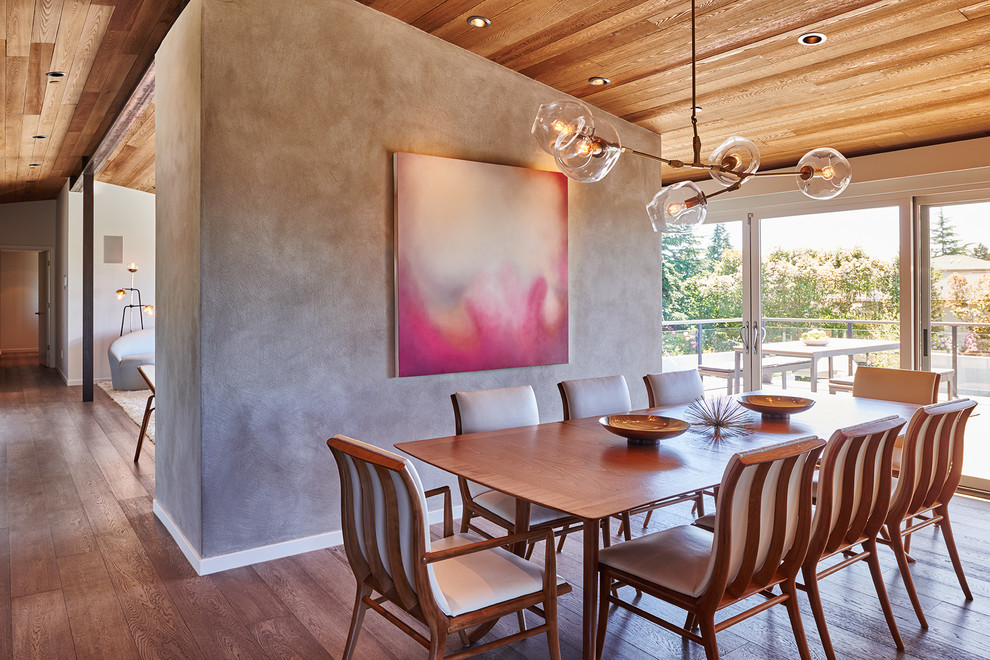 Foto di una grande sala da pranzo aperta verso il soggiorno minimalista con pareti grigie, pavimento in legno massello medio e cornice del camino in intonaco
