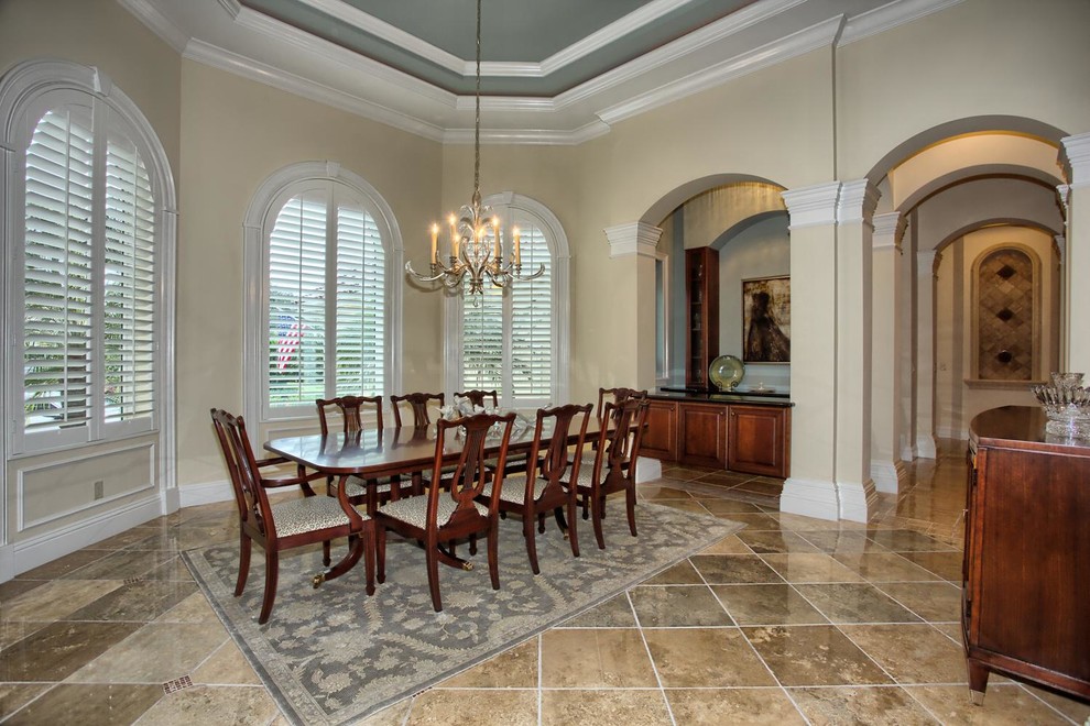 Example of a large classic travertine floor dining room design in Miami with yellow walls and no fireplace