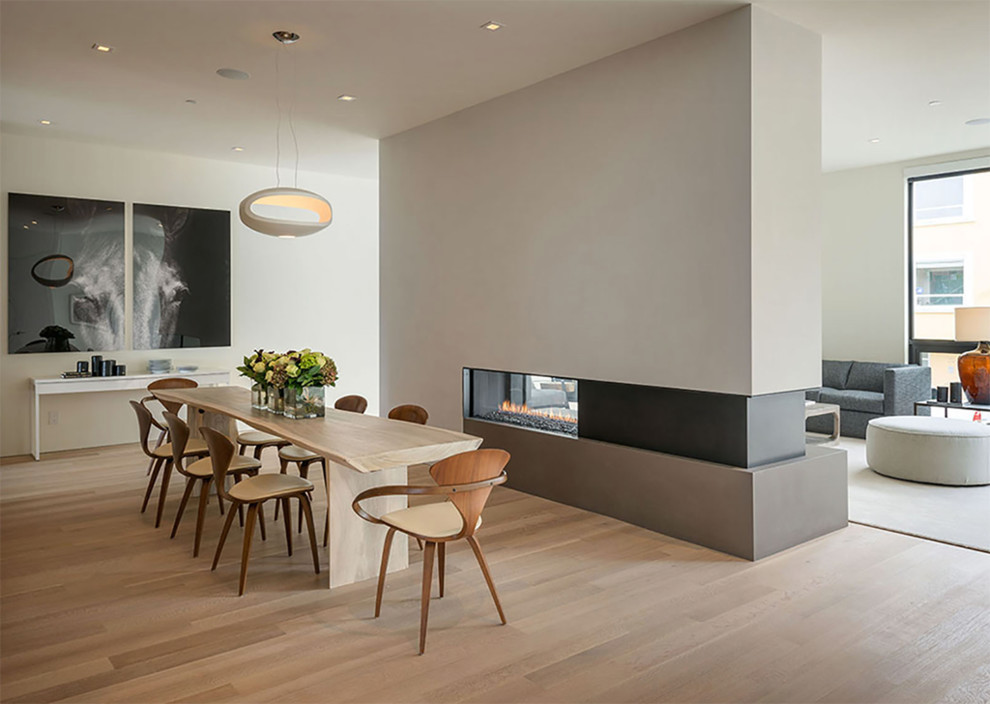 Imagen de comedor minimalista con paredes beige, suelo de madera clara y chimenea de doble cara
