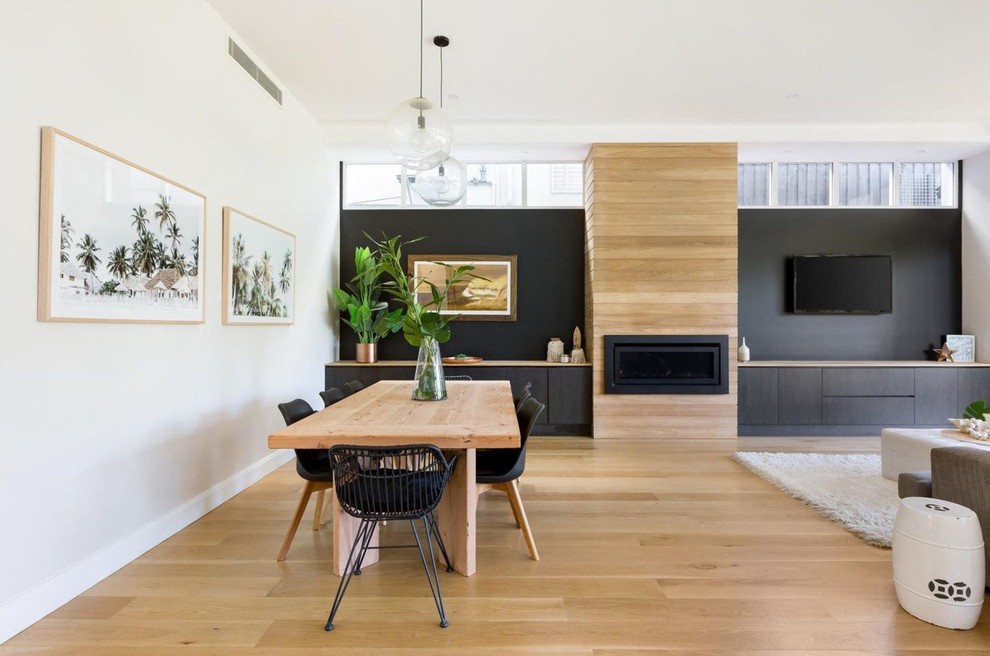 Modernes Esszimmer mit schwarzer Wandfarbe, hellem Holzboden, Gaskamin, Kaminumrandung aus Holz und braunem Boden in Sydney