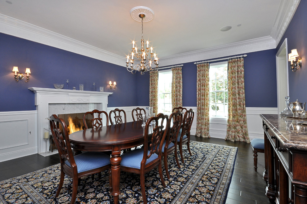 Cette photo montre une grande salle à manger chic fermée avec parquet foncé, une cheminée standard, un manteau de cheminée en pierre et un mur bleu.