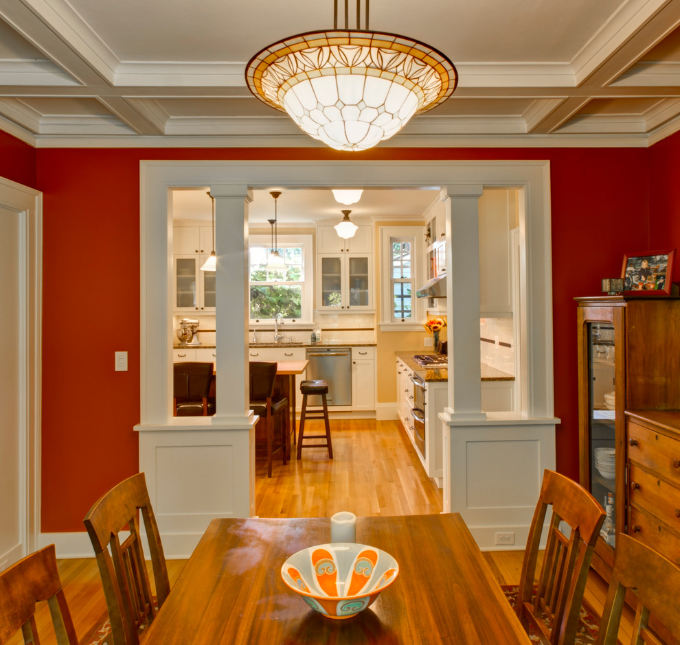 Aménagement d'une salle à manger craftsman fermée avec un mur rouge et un sol en bois brun.