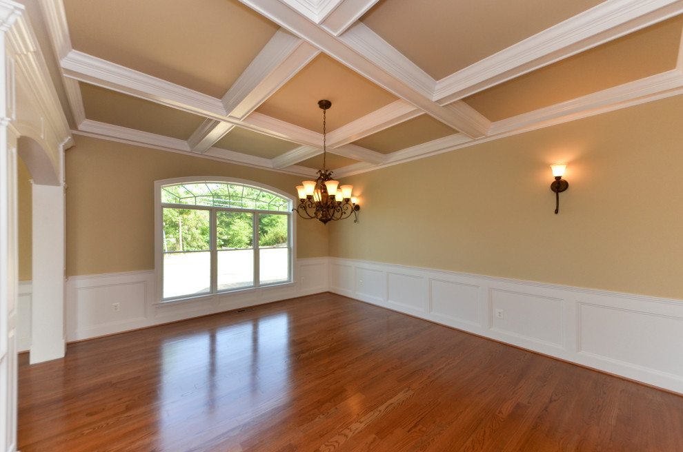 Foto di una sala da pranzo chiusa con pareti beige, pavimento in legno massello medio, nessun camino, pavimento marrone, soffitto a cassettoni e boiserie