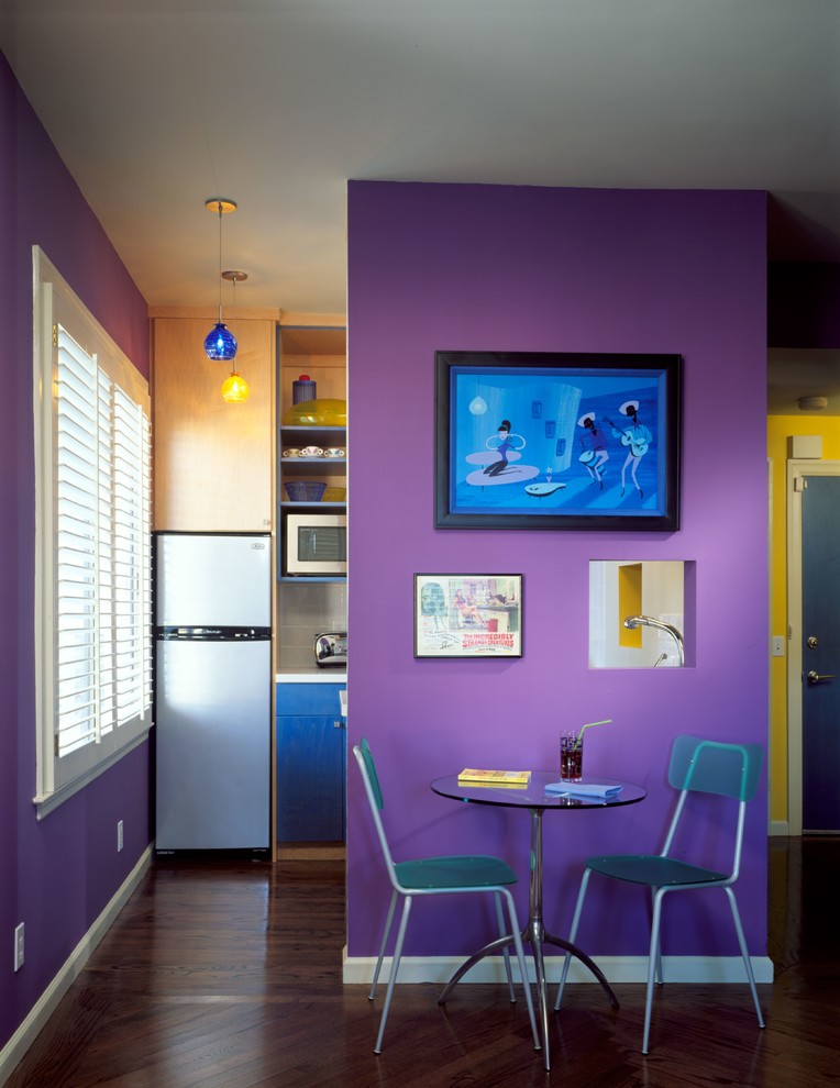 Cette image montre une petite salle à manger ouverte sur la cuisine design avec un mur violet, un sol en bois brun et un sol marron.