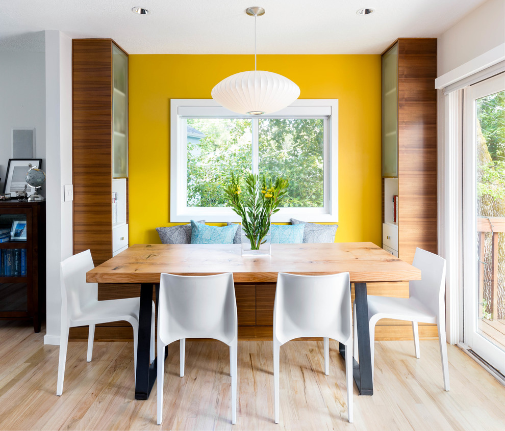 Immagine di una sala da pranzo aperta verso il soggiorno minimal di medie dimensioni con pareti gialle, parquet chiaro e nessun camino