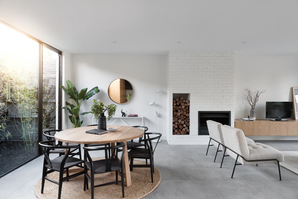 Cette image montre une salle à manger ouverte sur le salon design avec un mur blanc, une cheminée ribbon, un manteau de cheminée en brique et un sol gris.