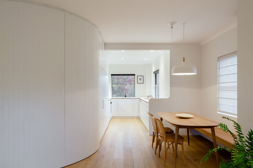 Foto di una sala da pranzo aperta verso la cucina minimalista con pareti bianche e parquet chiaro