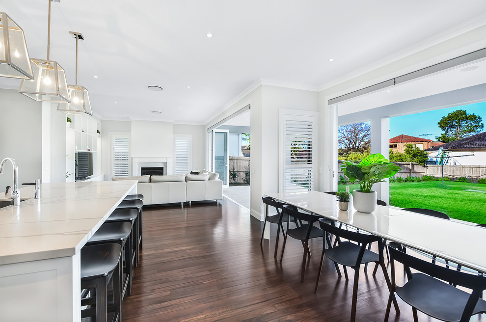Inspiration for a large contemporary open plan dining room in Sydney with white walls, a standard fireplace, brown floors, a brick fireplace surround and dark hardwood flooring.