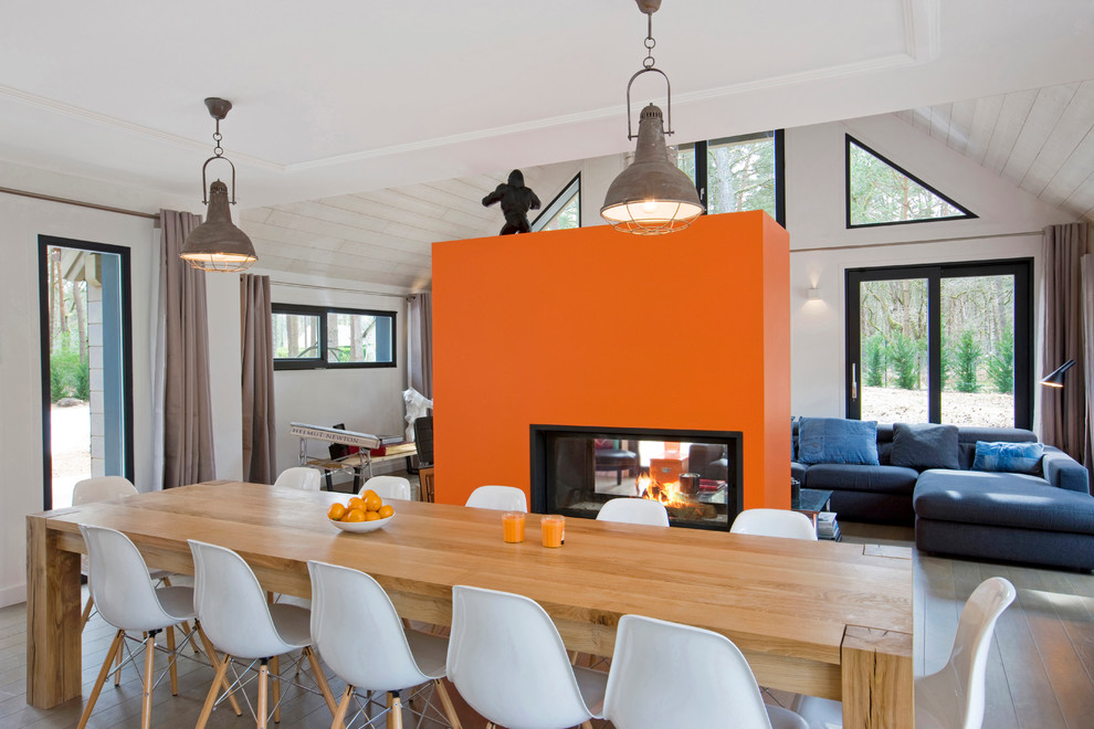 Immagine di una grande sala da pranzo aperta verso il soggiorno contemporanea con pareti arancioni e parquet chiaro