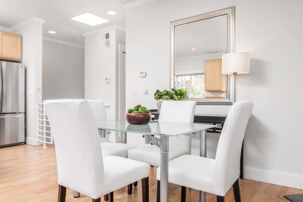 Cette image montre une petite salle à manger ouverte sur la cuisine design avec un mur blanc et parquet clair.