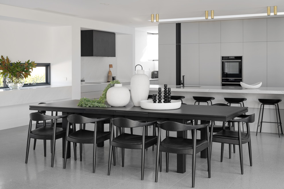 Cette image montre une salle à manger ouverte sur la cuisine design avec un mur blanc et un sol gris.