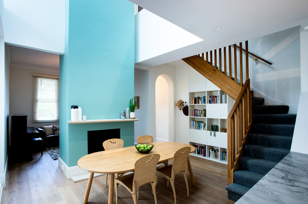 Cette image montre une salle à manger design avec une cheminée standard, un mur blanc, un sol en bois brun et un sol beige.