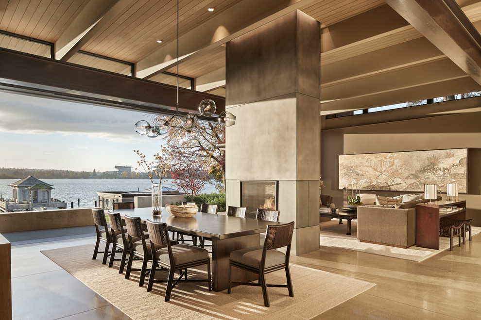 Cette photo montre une salle à manger ouverte sur le salon tendance avec sol en béton ciré, une cheminée double-face, un manteau de cheminée en béton et un sol gris.