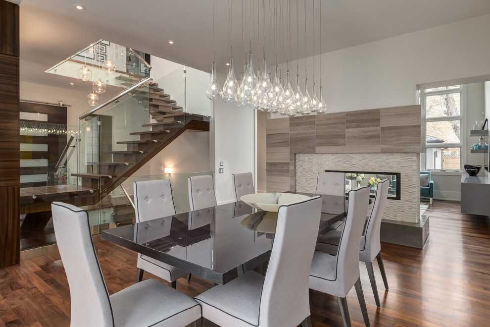 Idées déco pour une salle à manger moderne avec un mur blanc, un sol en bois brun, une cheminée double-face et un manteau de cheminée en carrelage.