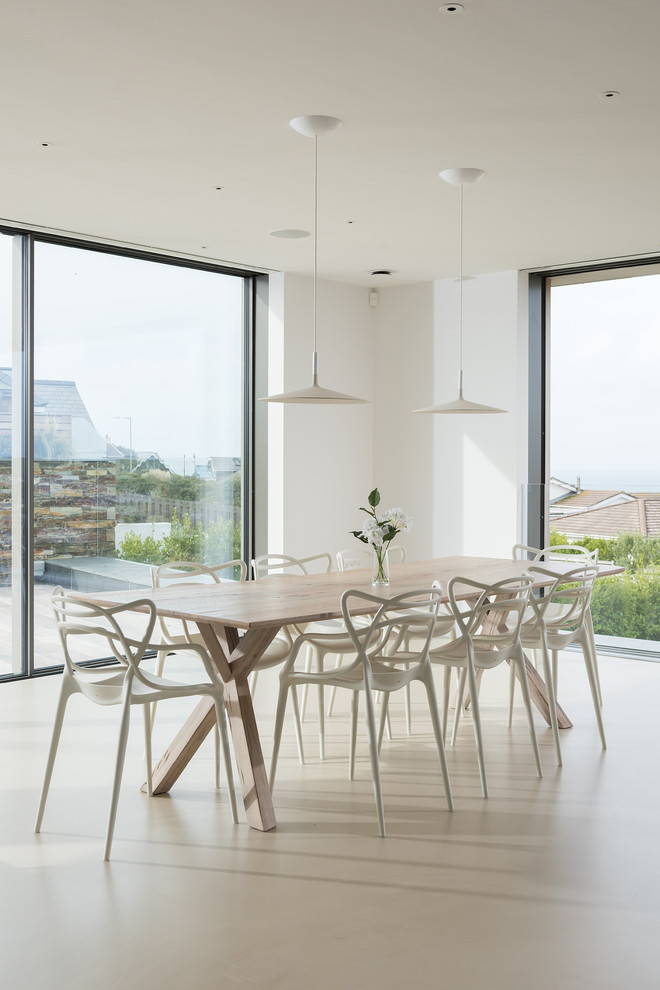 Large contemporary open plan dining room in Cornwall with concrete flooring, beige floors and white walls.