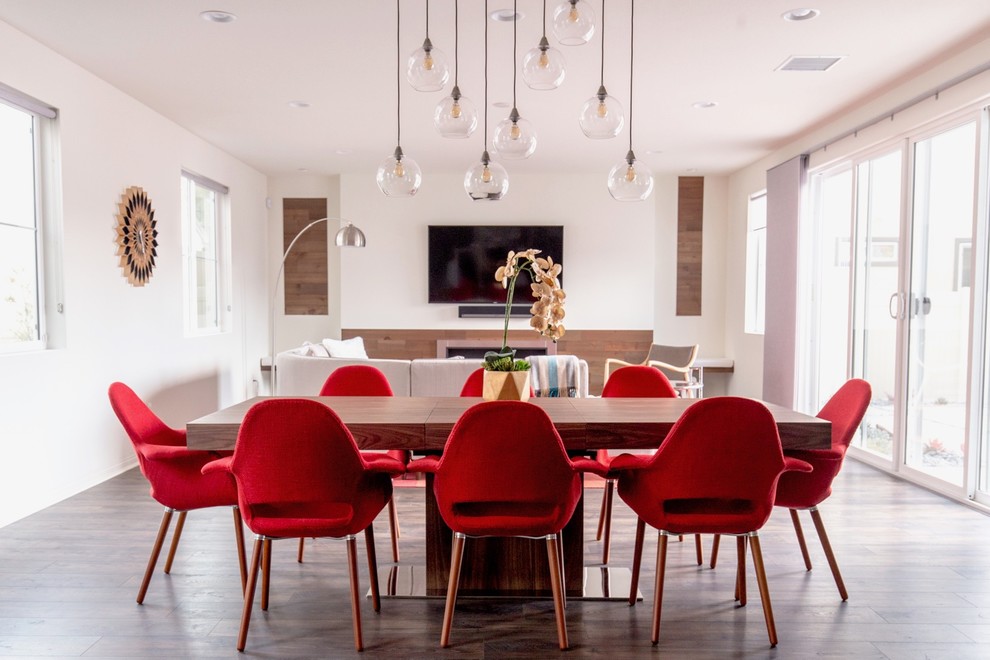 Cette photo montre une salle à manger ouverte sur le salon tendance avec un mur blanc, parquet foncé, une cheminée standard et un sol marron.