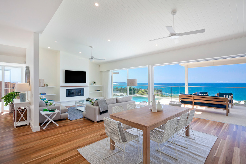 Example of a large beach style medium tone wood floor great room design in Sunshine Coast with white walls, a standard fireplace and a wood fireplace surround