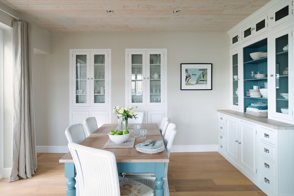 Inspiration for a coastal enclosed dining room in Other with beige walls, light hardwood flooring, a wood burning stove, a wooden fireplace surround and brown floors.