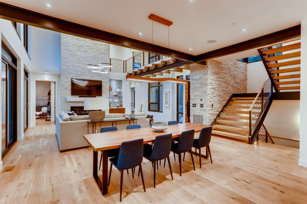 Inspiration for a large modern open plan dining room in Denver with light hardwood flooring, a ribbon fireplace, a stone fireplace surround, brown floors and exposed beams.