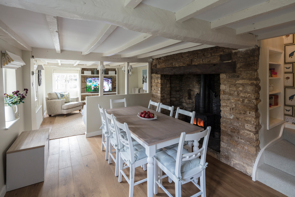 This is an example of a small farmhouse dining room in Gloucestershire with beige walls, medium hardwood flooring, a wood burning stove and beige floors.