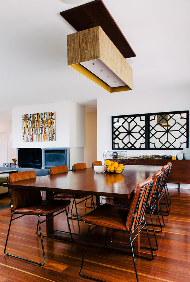 Inspiration pour une salle à manger ouverte sur le salon design avec un mur blanc, un sol en bois brun et une cheminée standard.