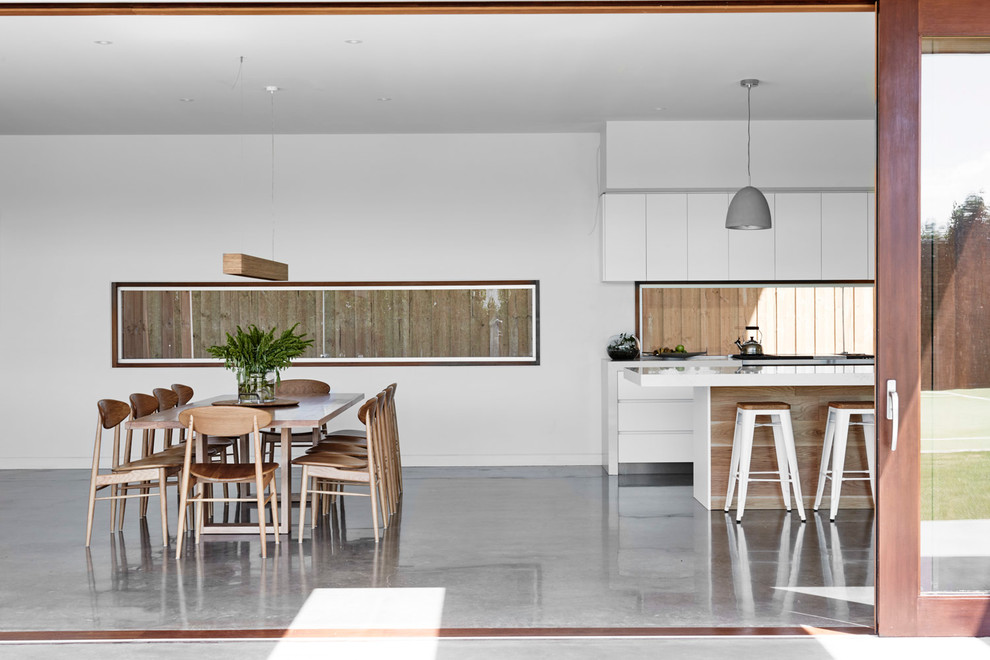 Aménagement d'une salle à manger contemporaine avec un mur blanc et sol en béton ciré.