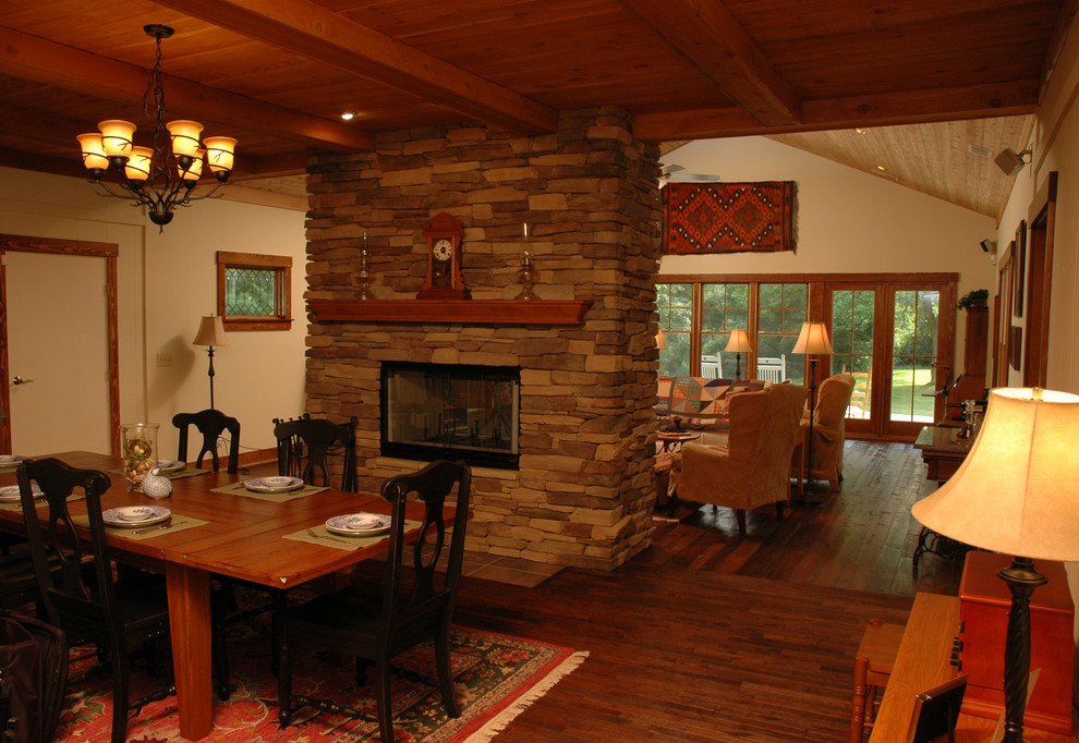 Ejemplo de comedor de estilo americano de tamaño medio abierto con paredes beige, suelo de madera en tonos medios, chimenea de doble cara y marco de chimenea de piedra