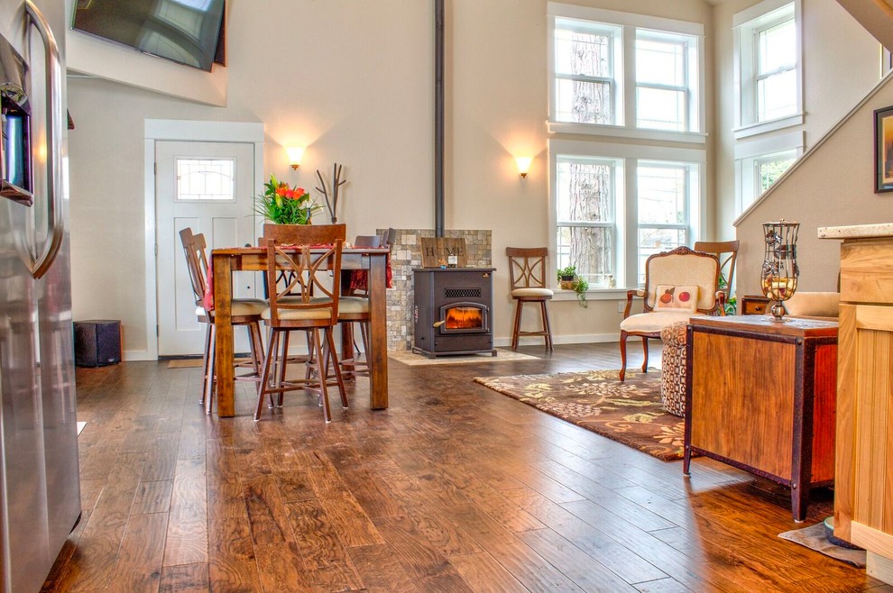 Immagine di una piccola sala da pranzo aperta verso il soggiorno stile americano con pareti grigie, pavimento in legno massello medio, stufa a legna e pavimento marrone
