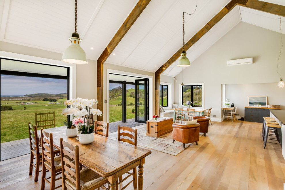 Foto di una sala da pranzo aperta verso il soggiorno country con pareti grigie, pavimento in legno massello medio, pavimento marrone e soffitto a volta