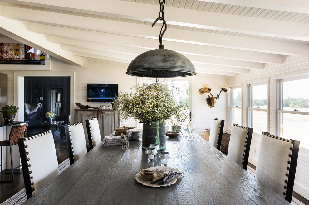 Cette photo montre une grande salle à manger ouverte sur le salon nature avec un mur blanc, parquet foncé, un sol marron, une cheminée standard et un manteau de cheminée en béton.