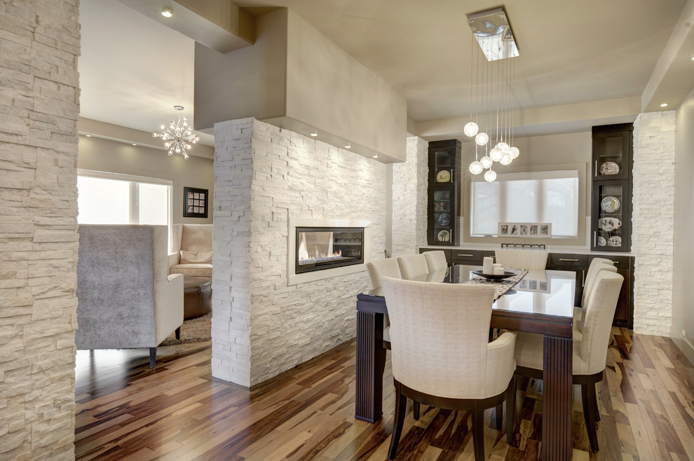 Cette photo montre une salle à manger moderne de taille moyenne avec un mur beige, un sol en bois brun, une cheminée double-face et un manteau de cheminée en pierre.