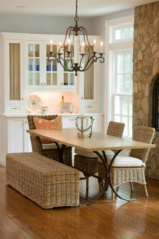 Cette photo montre une salle à manger ouverte sur la cuisine nature de taille moyenne avec un mur gris, un sol en bois brun, une cheminée standard, un manteau de cheminée en pierre et un sol marron.