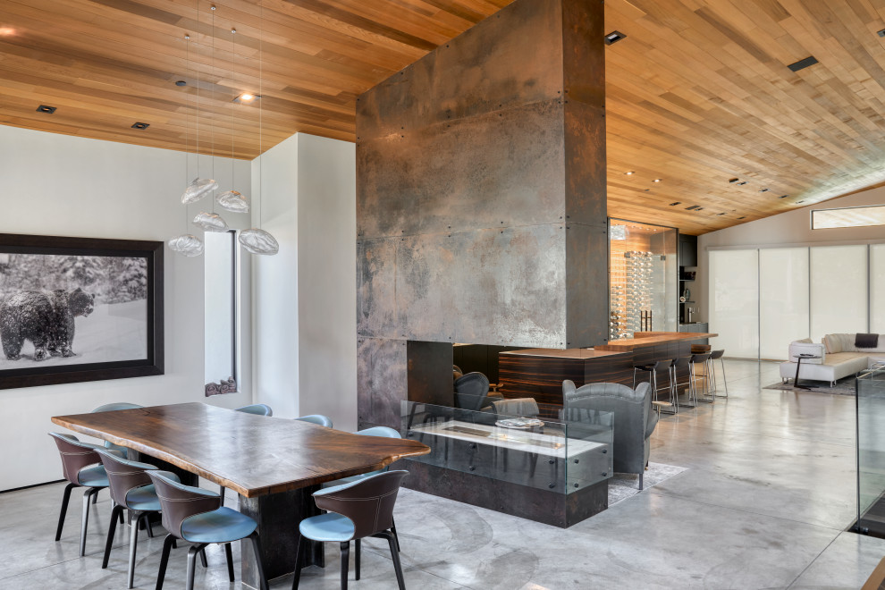 Réalisation d'une salle à manger minimaliste avec sol en béton ciré, une cheminée double-face et un manteau de cheminée en métal.