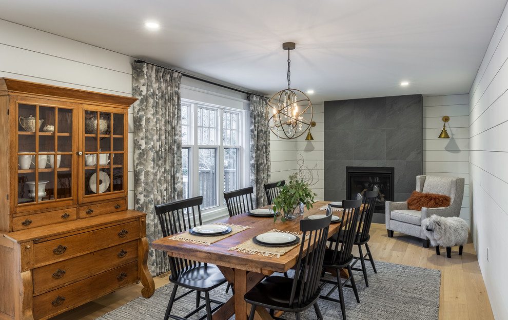 Photo of a farmhouse dining room in Toronto with white walls, light hardwood flooring, a standard fireplace, a tiled fireplace surround and brown floors.