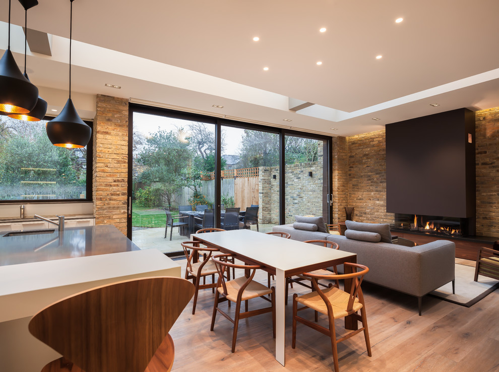 Design ideas for a medium sized contemporary open plan dining room in London with light hardwood flooring, a ribbon fireplace and beige floors.