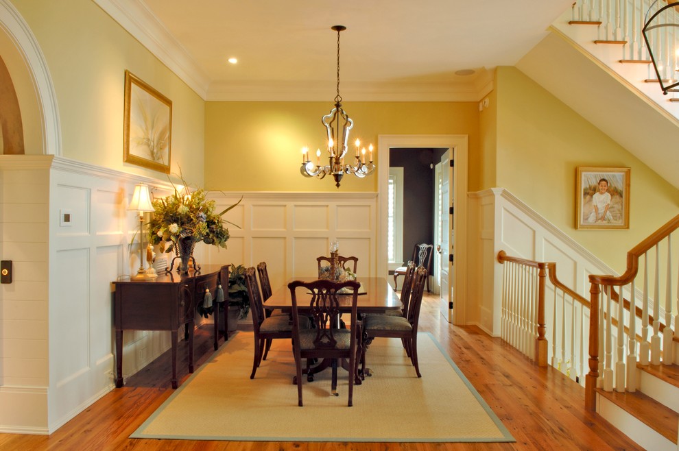 Geschlossenes, Mittelgroßes Klassisches Esszimmer ohne Kamin mit gelber Wandfarbe, hellem Holzboden, braunem Boden und vertäfelten Wänden in Charleston