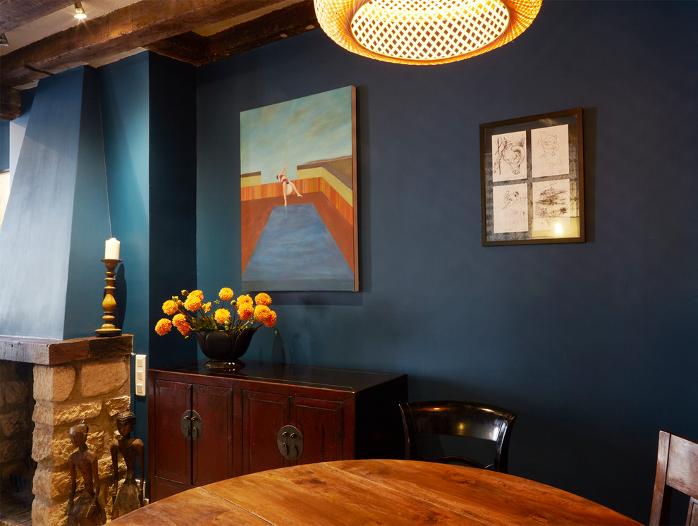 Modelo de comedor ecléctico pequeño con paredes azules, suelo de madera clara y marco de chimenea de madera