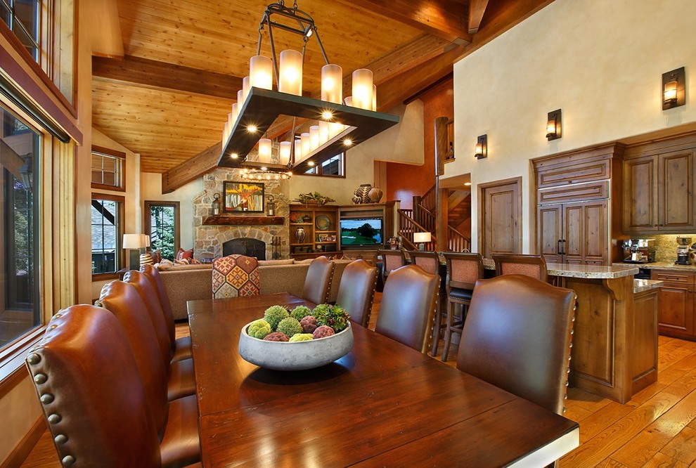 Inspiration pour une très grande salle à manger ouverte sur le salon sud-ouest américain avec un sol en bois brun, une cheminée standard, un manteau de cheminée en pierre et un mur beige.