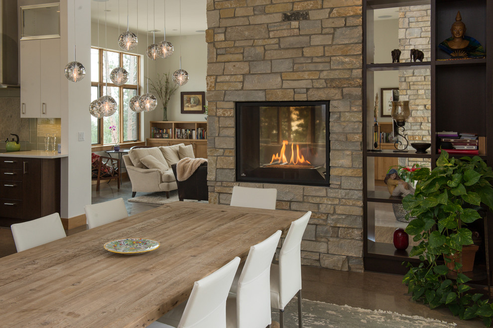 Idée de décoration pour une salle à manger ouverte sur la cuisine design avec une cheminée double-face et un manteau de cheminée en pierre.