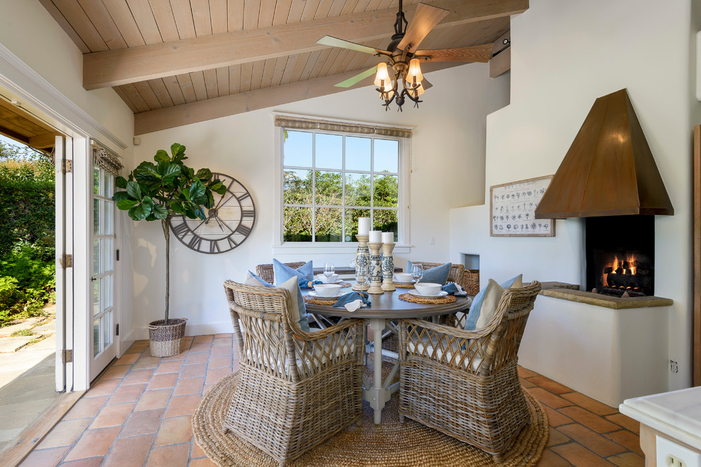 This is an example of a nautical dining room in Santa Barbara with white walls, terracotta flooring, a standard fireplace and orange floors.
