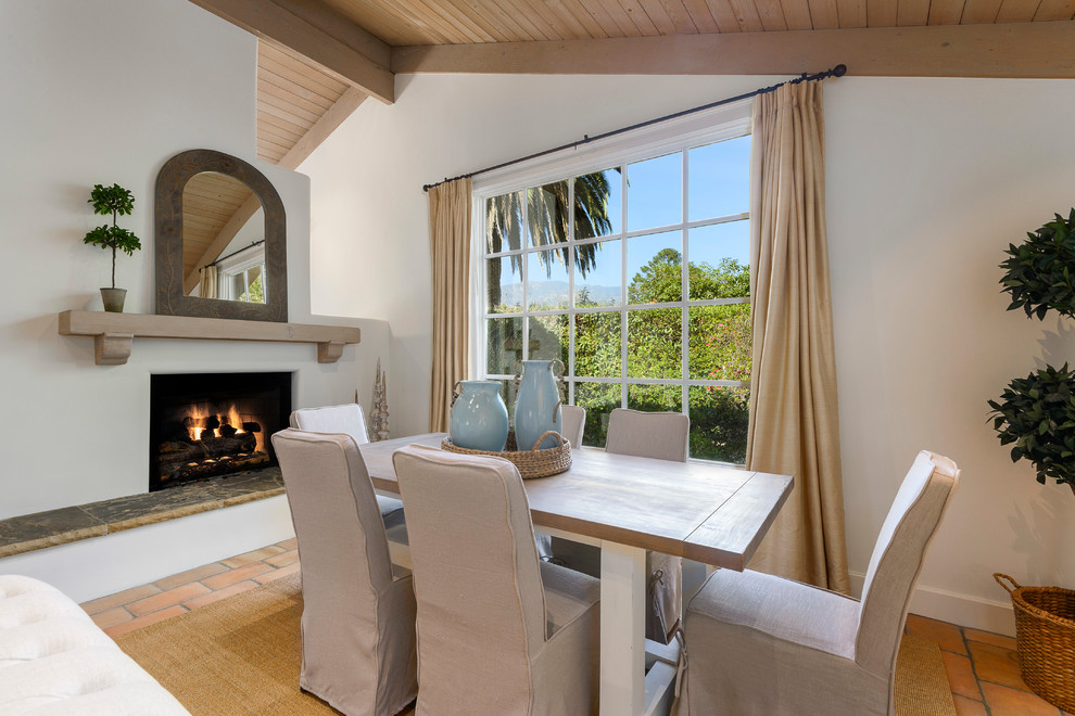 Example of a beach style terra-cotta tile and orange floor dining room design in Santa Barbara with white walls and a standard fireplace