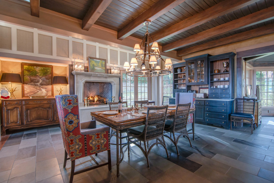 Cette image montre une grande salle à manger ouverte sur la cuisine rustique avec un mur beige, un sol en ardoise, cheminée suspendue, un manteau de cheminée en béton et un sol gris.