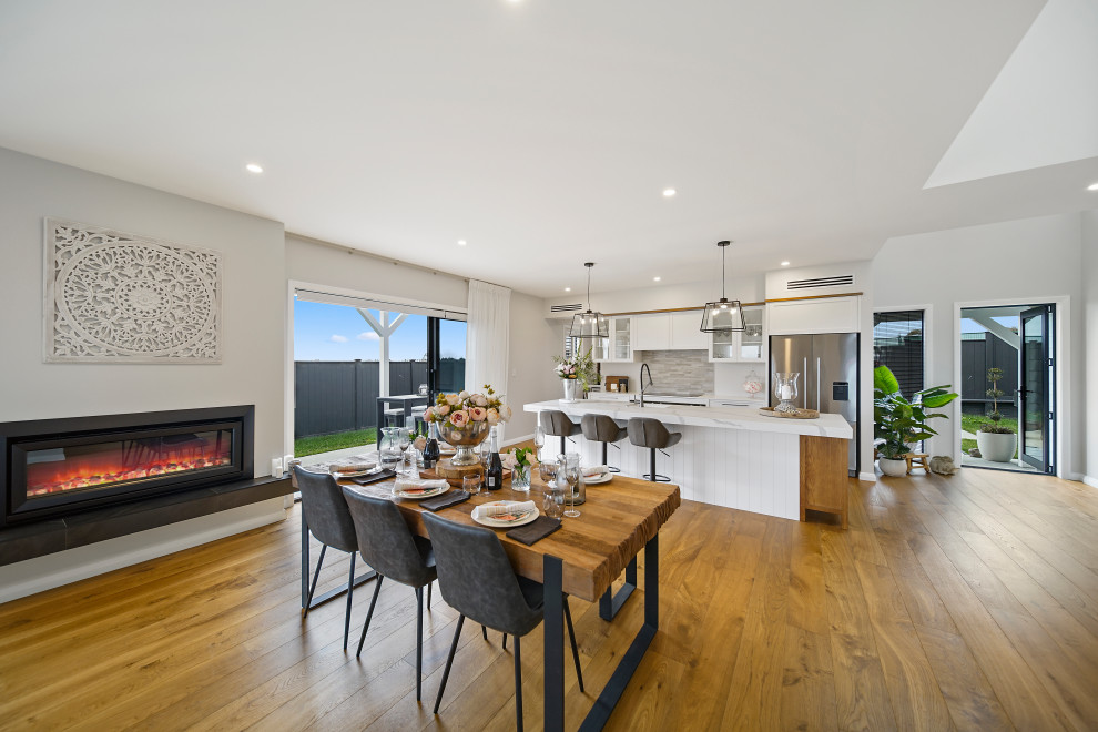 Kitchen/dining room combo - large rustic medium tone wood floor, brown floor and vaulted ceiling kitchen/dining room combo idea in Auckland with white walls, a hanging fireplace and a tile fireplace